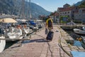 Tourist with a suitcase and a backpack walks along the yachts and motorboats moored at the pier.